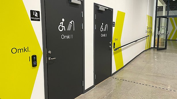 Två dörrar med en stiliserad bild av en person i rullstol som duschar.