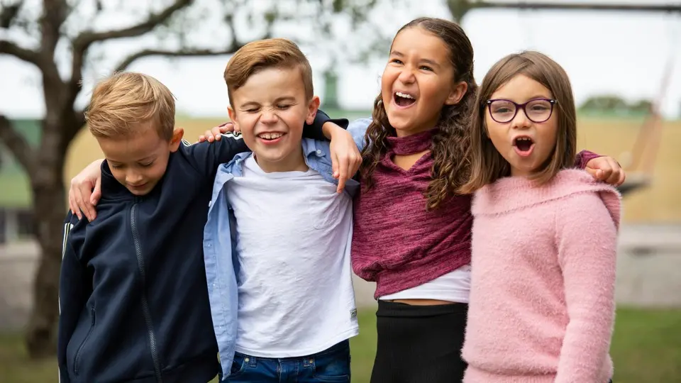 Fyra barn krokar arm utanför en skola.