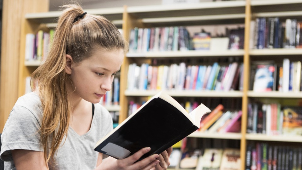 Bilden visar en ung tjej på biblioteket som läser en bok