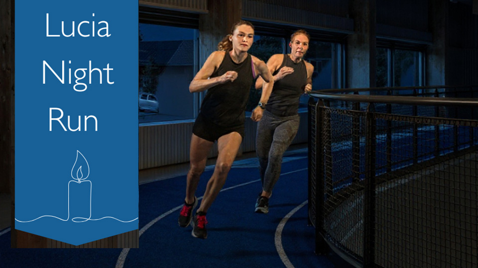 Två kvinnor i träningskläder springer mycket fort på en löpbana inomhus.