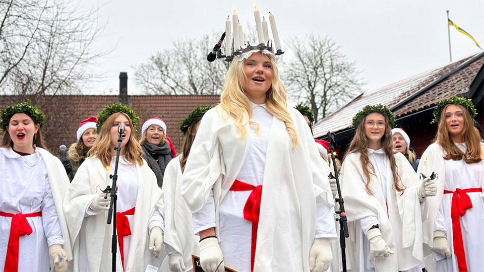 En gruppbild med vitklädd lucia främst med ljuskrona. Runt henne står tärnor. Alla sjunger.