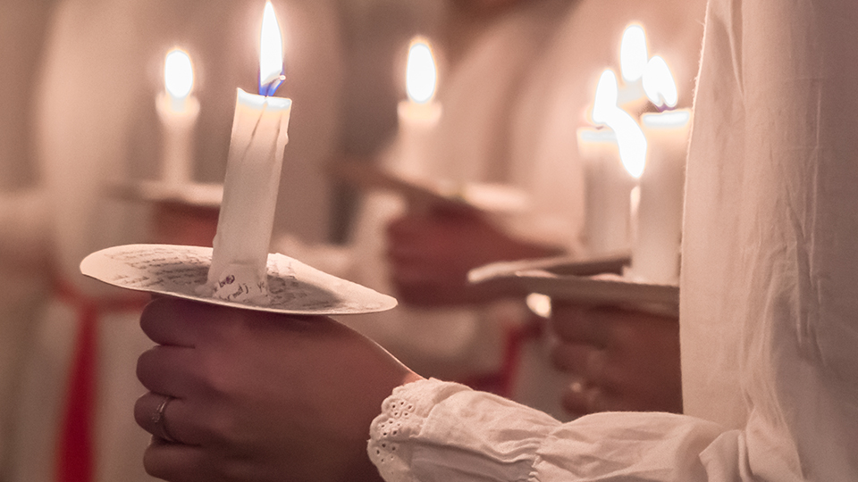 En närbild på flera händer som håller varsitt ljus. Man kan se att de är klädda i vitt.