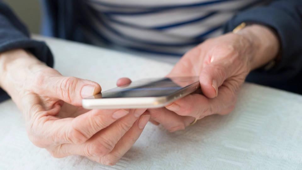 Två händer håller i en mobiltelefon ovanför ett vitt bord.