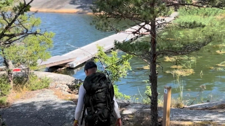 En man med ryggsäck vandrar i skärgårdsmiljö.