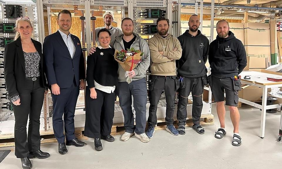 En grupp personer står uppställda framför kameran i företagsmiljö.