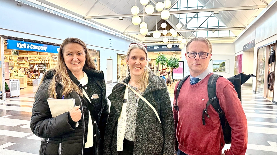 Personporträtt på tjänstemän i Åkersberga centrum. Tre personer står på rad. I bakgrunden syns flera butiker i Åkersberga centrum.