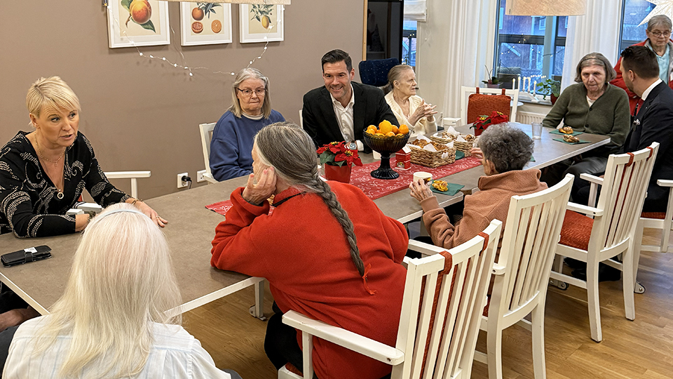 Ministrarna Anna Tenje och Johan Forsell sitter vid ett bord tillsammans med äldre boende på Attendo Kantarellvägen.