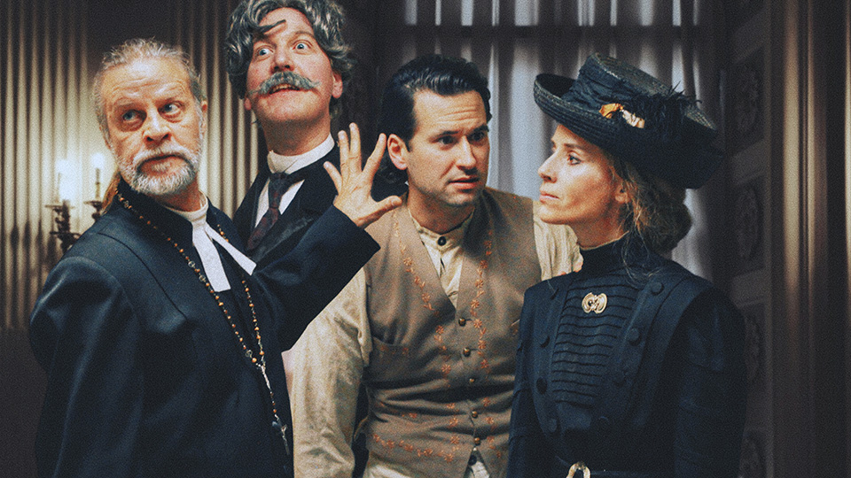 Tre män och en kvinna, alla i kläder från förra sekelskiftet. De stirrar alla åt olika håll.