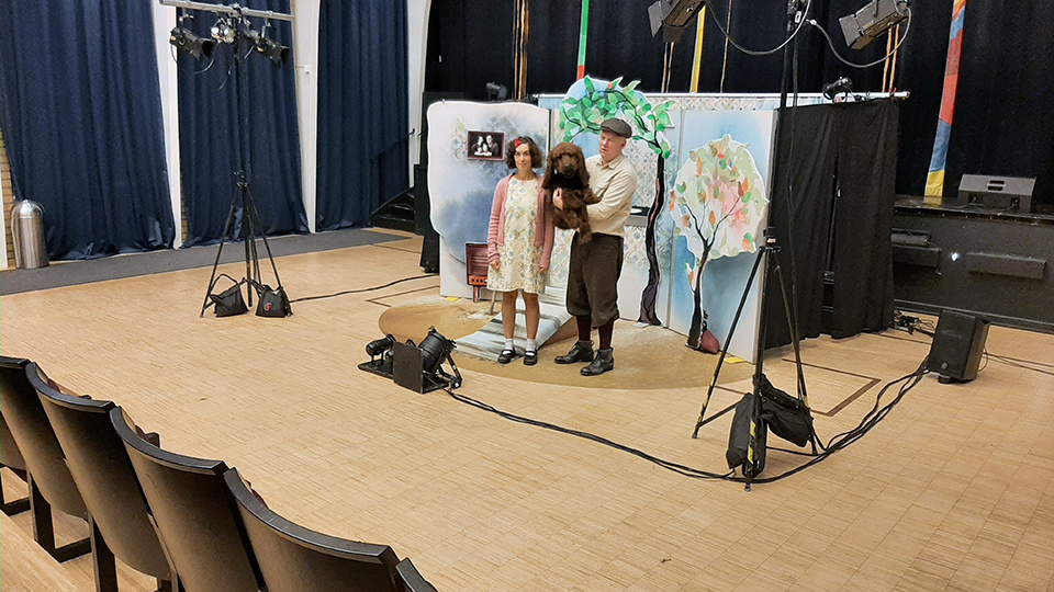 Två skådespelare på scengolvet innan publiken släpps in. En är klädd som en liten flicka och en man håller en låtsashund.