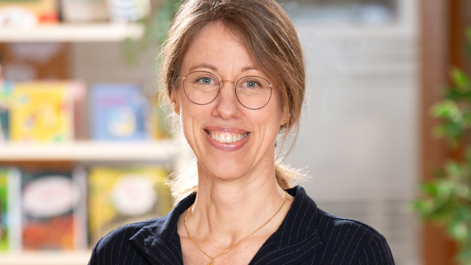 Ett porträttfoto av en blond kvinna med stort leende och runda, stålbågade glasögon.