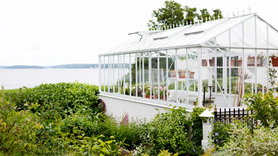 Ett fristående inglasat uterum i en vacker trädgård med utsikt mot havet