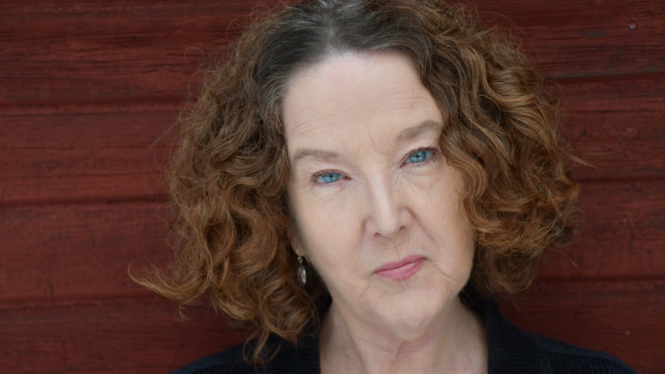 Ett porträttfoto av en kvinna med lockigt, rött hår och kisande ögon.