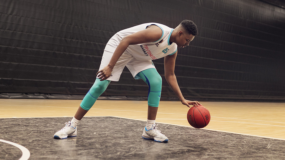 En ung man i träningskläder studsar en basketboll.