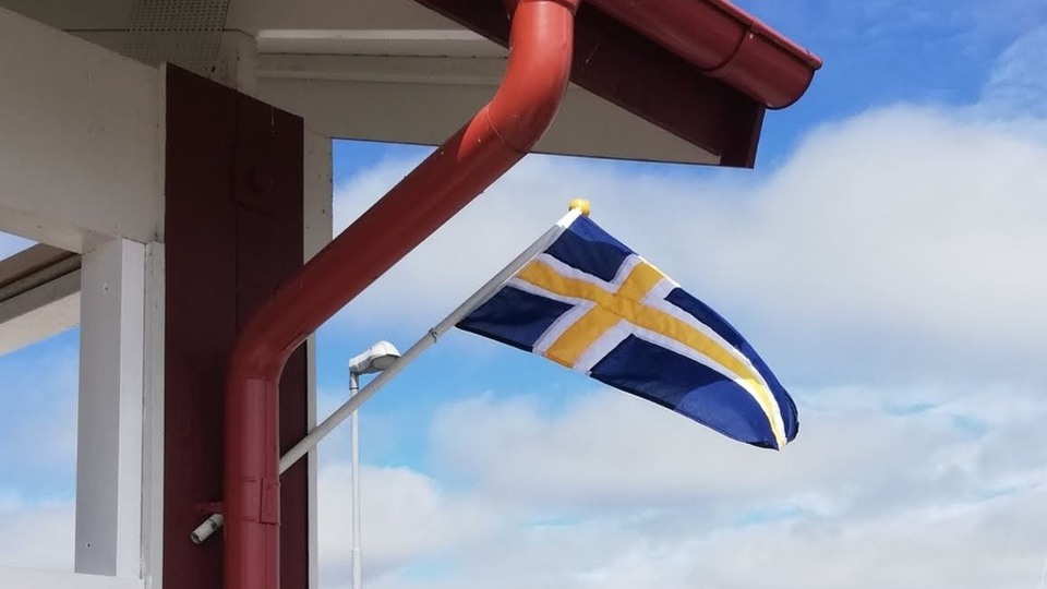 Bilden föreställer Roslagens flagga på ett röd hus med himlen som bakgrund.