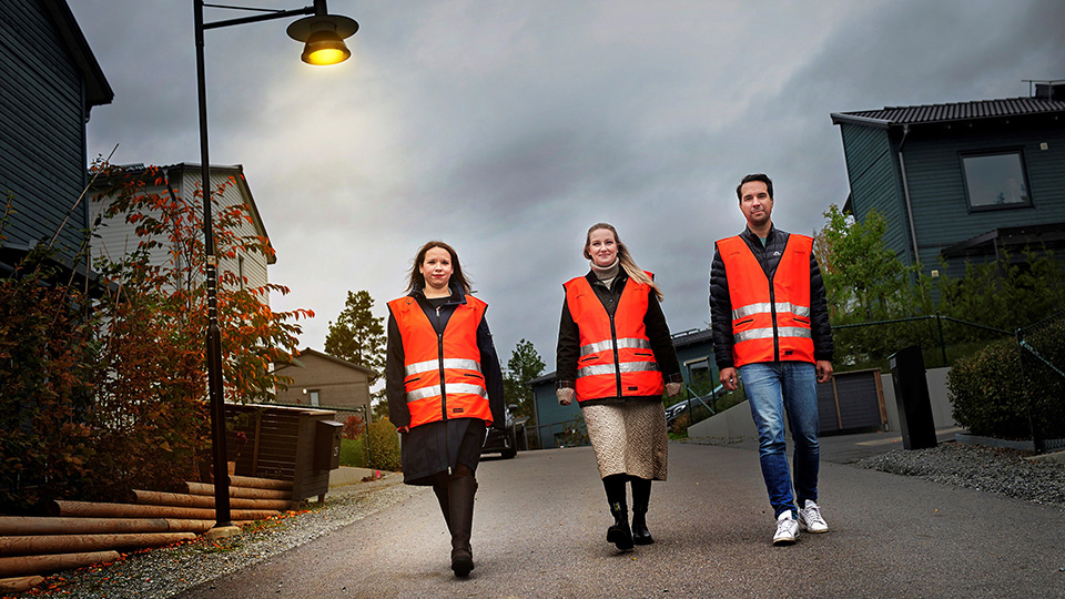 Bilden visar tre personer som nattvandrar. De går på led och bär röda västar.