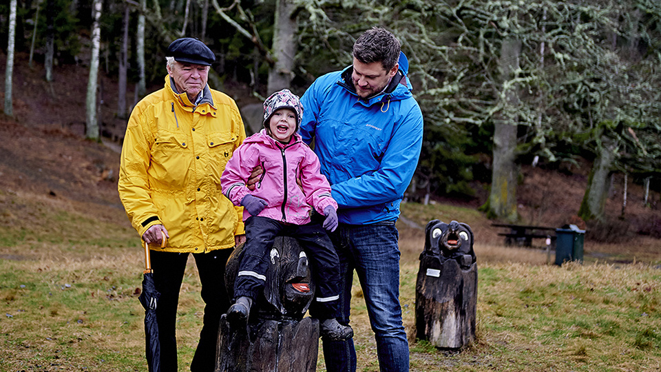 Två vuxna och ett barn leker i en naturlekplats