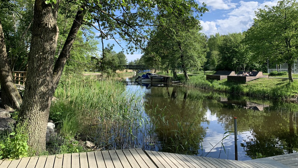 Vy över Åkers kanal med en brygga i förgrunden och sittplatser på andra sidan kanalen.