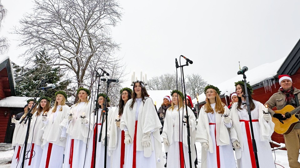 Bilden visar tärnor och Lucia som står på rad utomhus i ett snöigt vinterlandskap