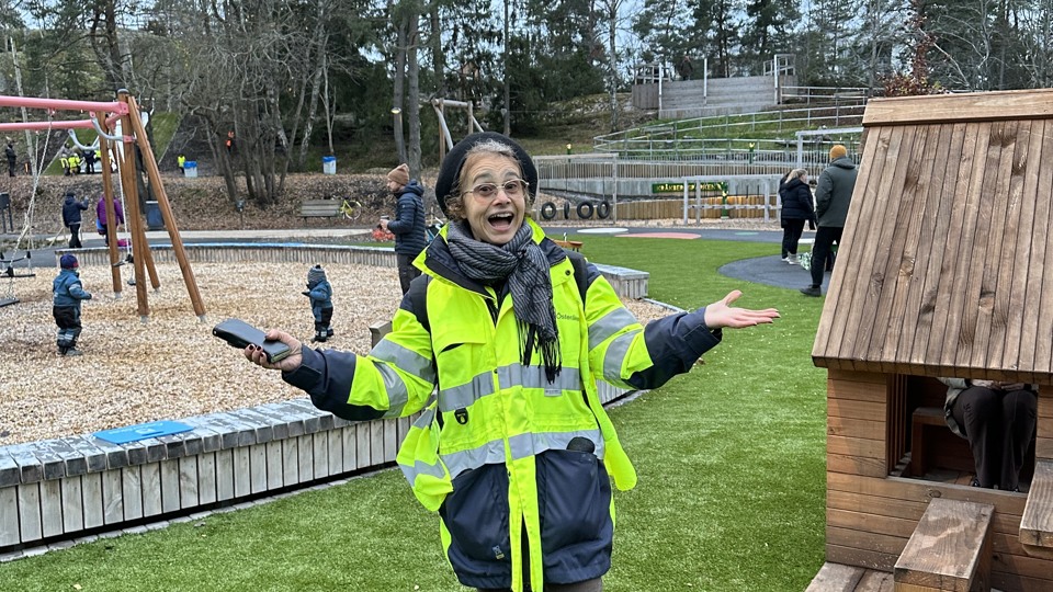 En person står i lekparken med utslagna armar och ser glad ut