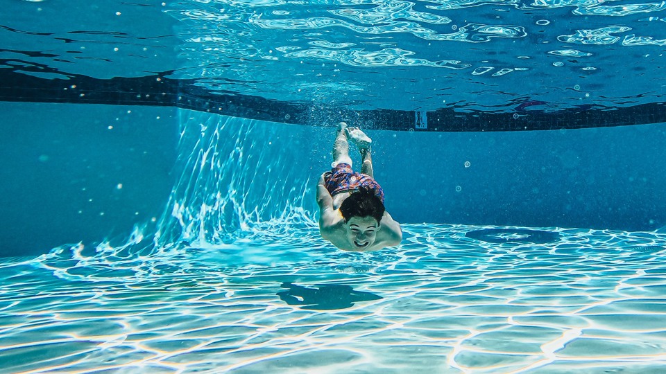 Barn simmar under vattnet i simbassäng.
