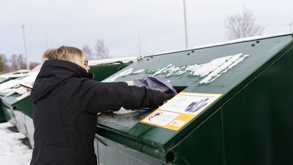 Bilden visar en kvinna som återvinner förpackningar en vinterdag