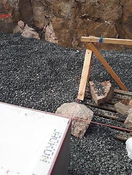 Byggarbetsplats med utsättningssnöre spänt mellan en vit byggkomponent och en träställning.