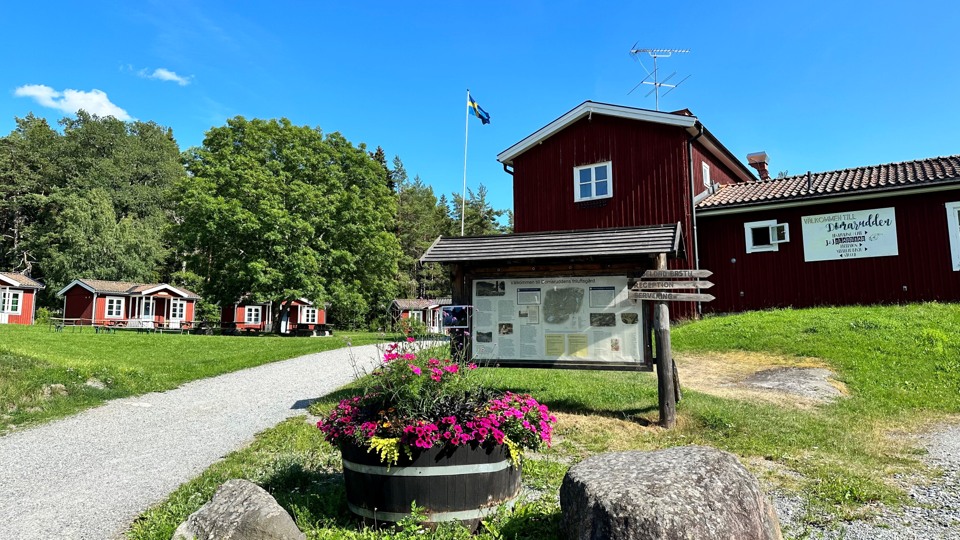 Domaruddens friluftsgård med röd huvudbyggnad och flera små gästhus en vacker sommardag.