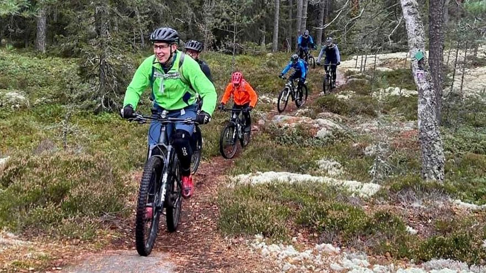 Fyra cyklister i färgglada regnställ cyklar i skogsterräng.