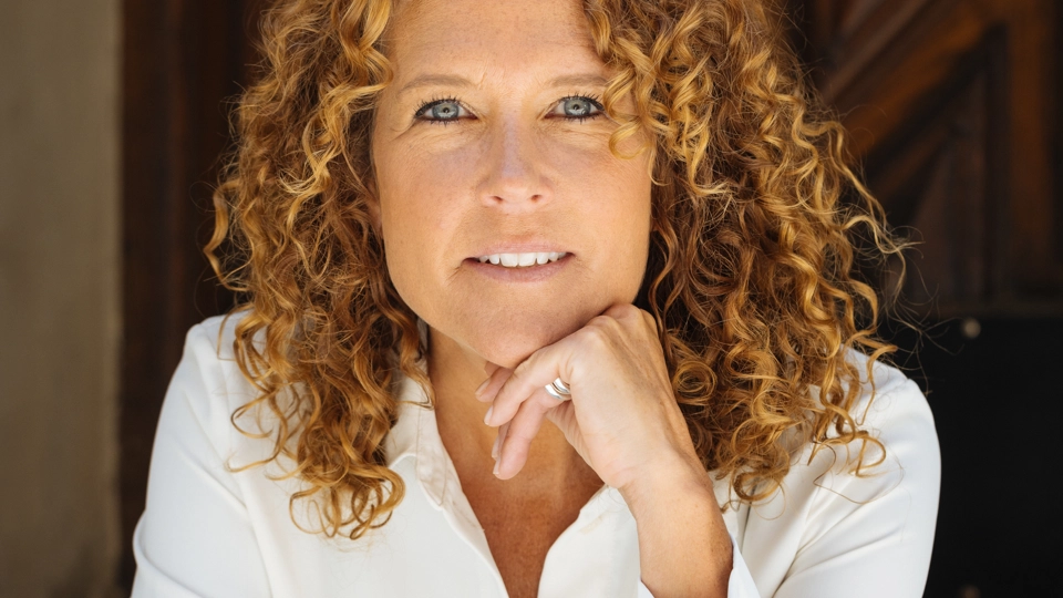 Anna sitter framåt lutad mot en mörk bakgrund, vit skjorta