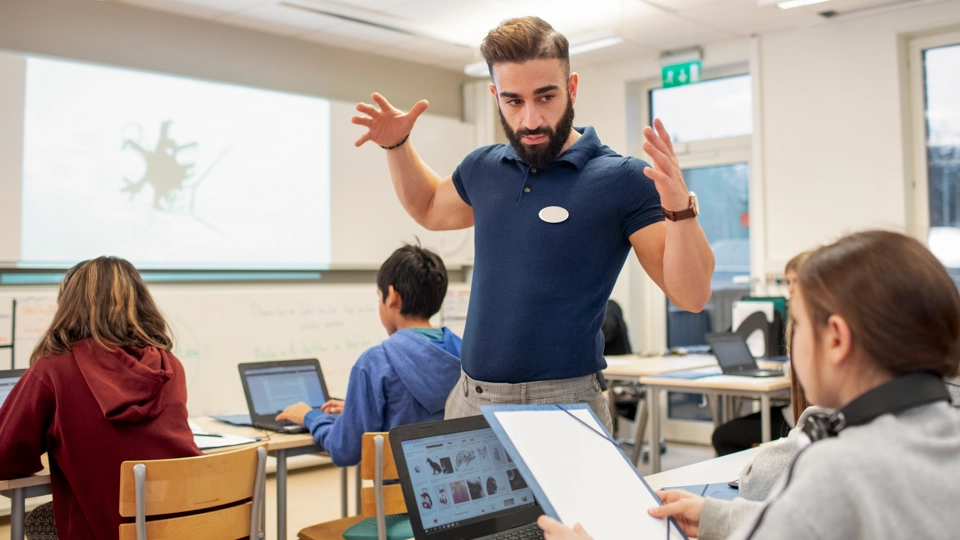 Engagerad lärare i klassrum gestikulerar med händerna för att förklara något.