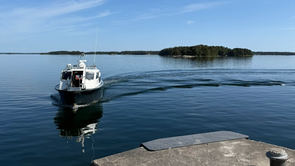 En mindre passagerarbåt på stilla havsvatten styr in mot en brygga.