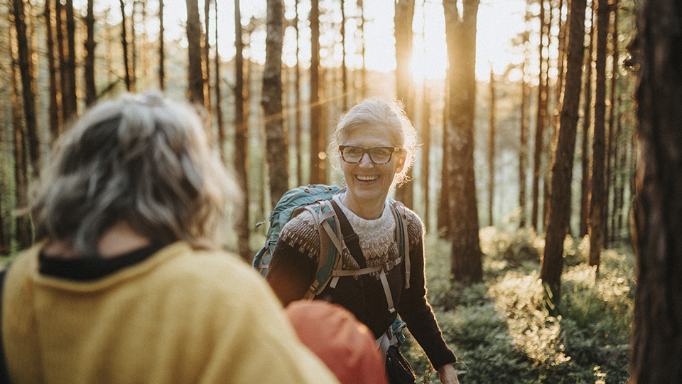 En mycket glad kvinna ler mot sitt sällskap som har ryggen mot kameran. De står i en skog med solljuset som strilas mellan träden.