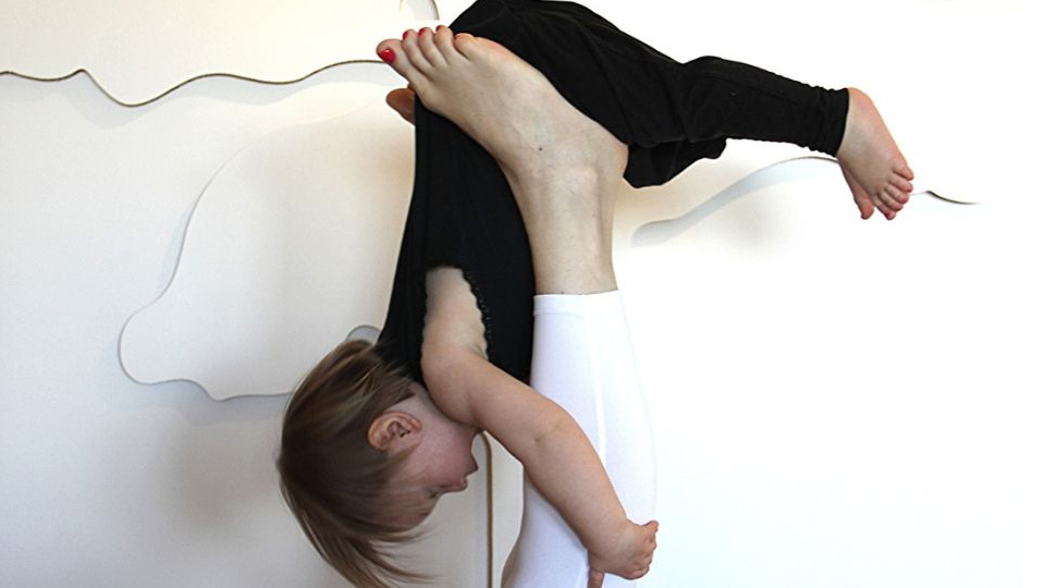 Ett litet barn lyfts upp i luften av en vuxens fötter.