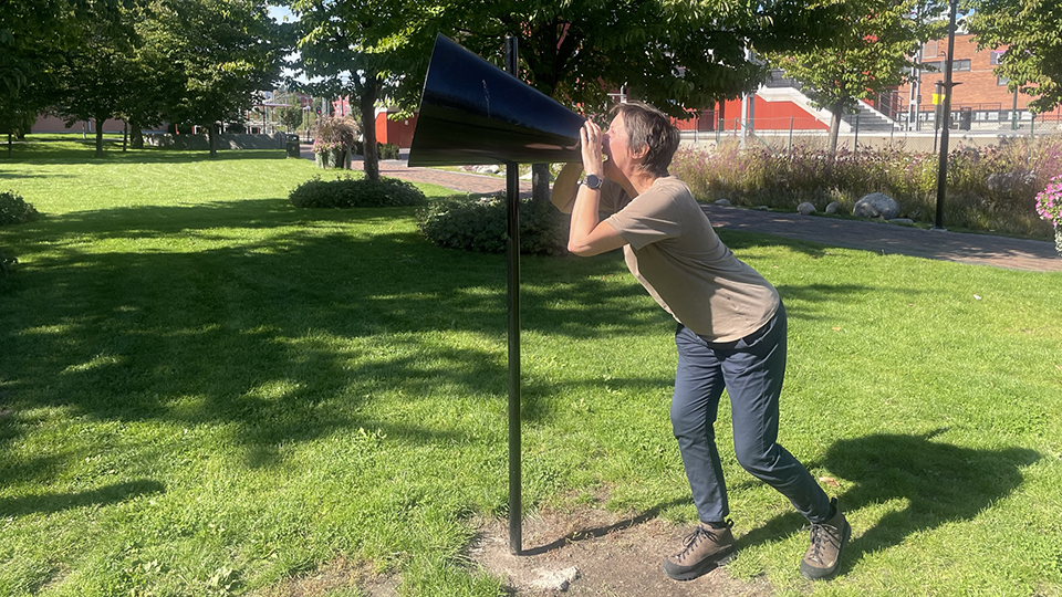 En person står och ropar i en megafon i en park.