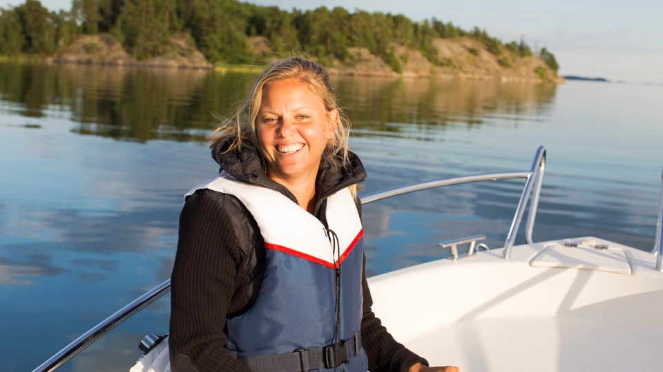 En tjej sitter med flytväst i en båt. Hon ler.