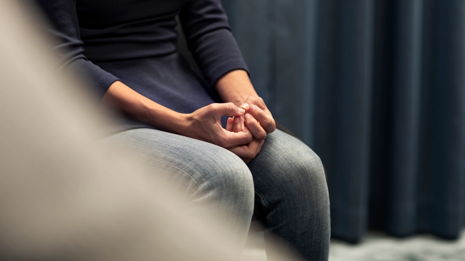 En ung person sitter på en stol med händerna i knät.