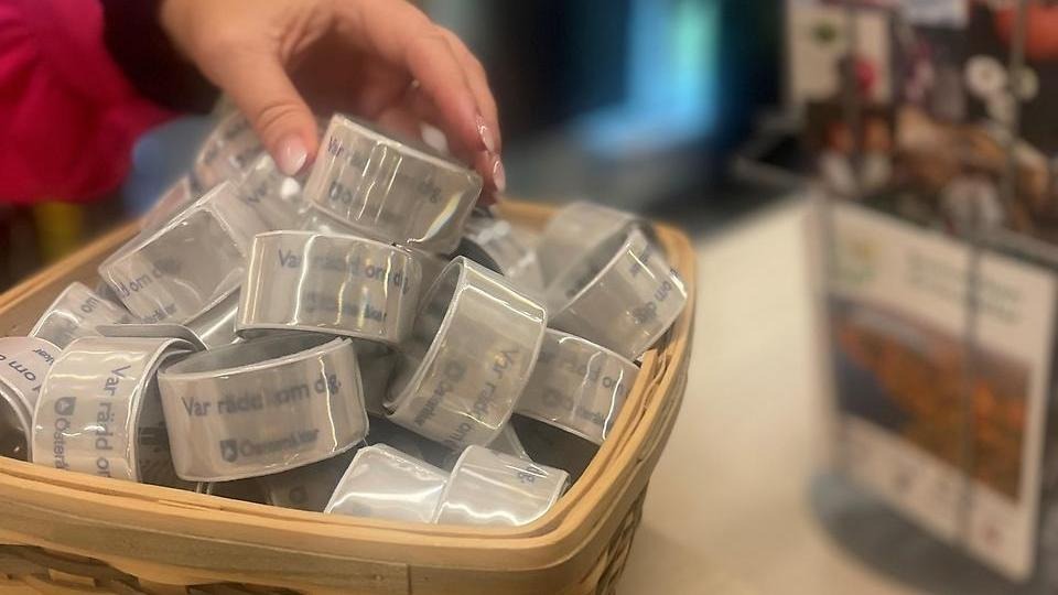 En korg med reflexer. En hand sträcker sig för att ta ett reflexband.