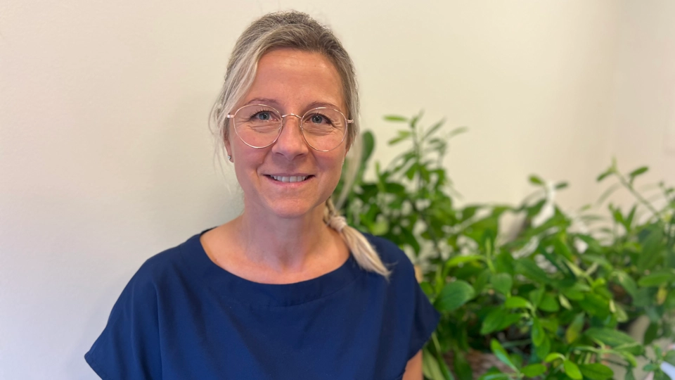 En kvinna i blå klänning står bredvid en krukväxt.