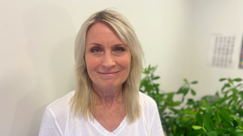 En kvinna står framför en krukväxt.