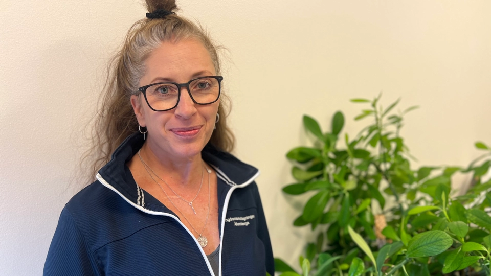 En kvinna med glasögon står bredvid en krukväxt.