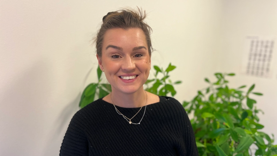 En kvinna står framför en krukväxt.