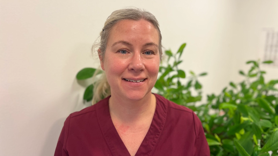 En kvinna i röd skjorta står framför en krukväxt.