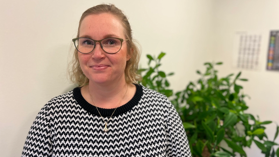 En kvinna med glasögon står framför en krukväxt.