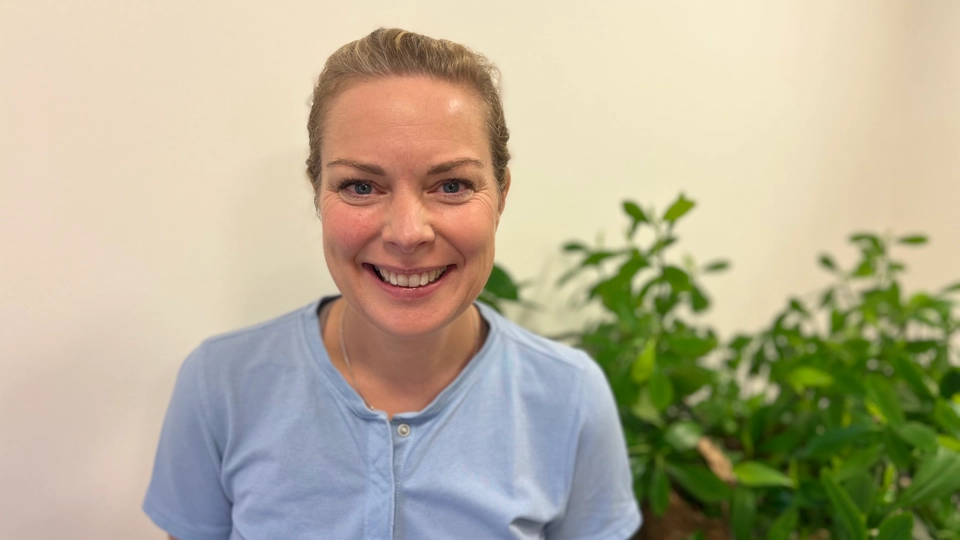 En kvinna står framför en krukväxt.