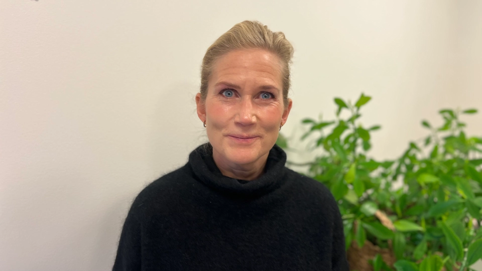 En kvinna står framför en krukväxt.