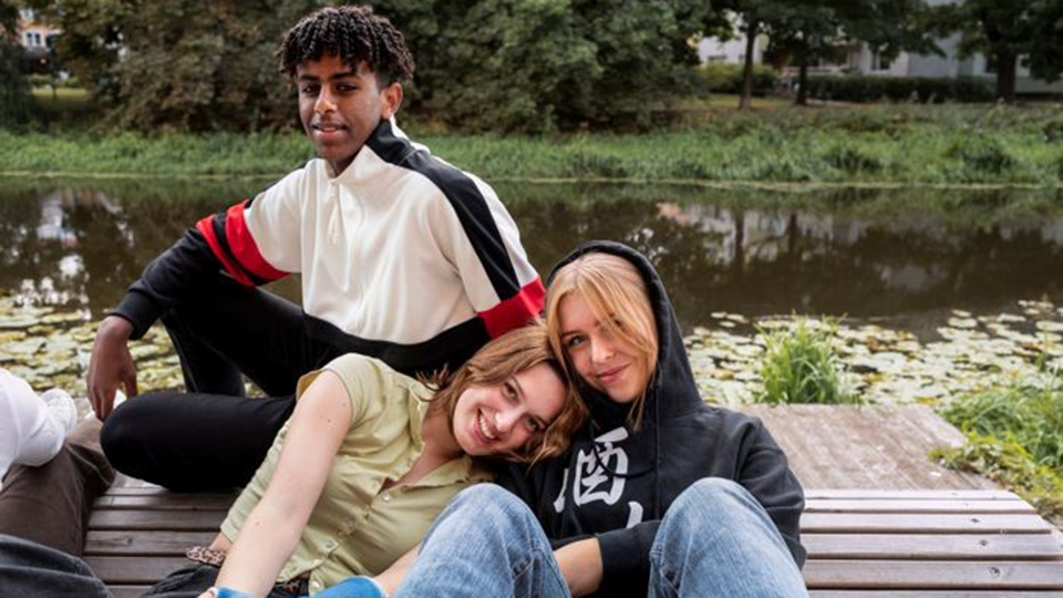 Tre glada ungdomar sitter på en brygga.