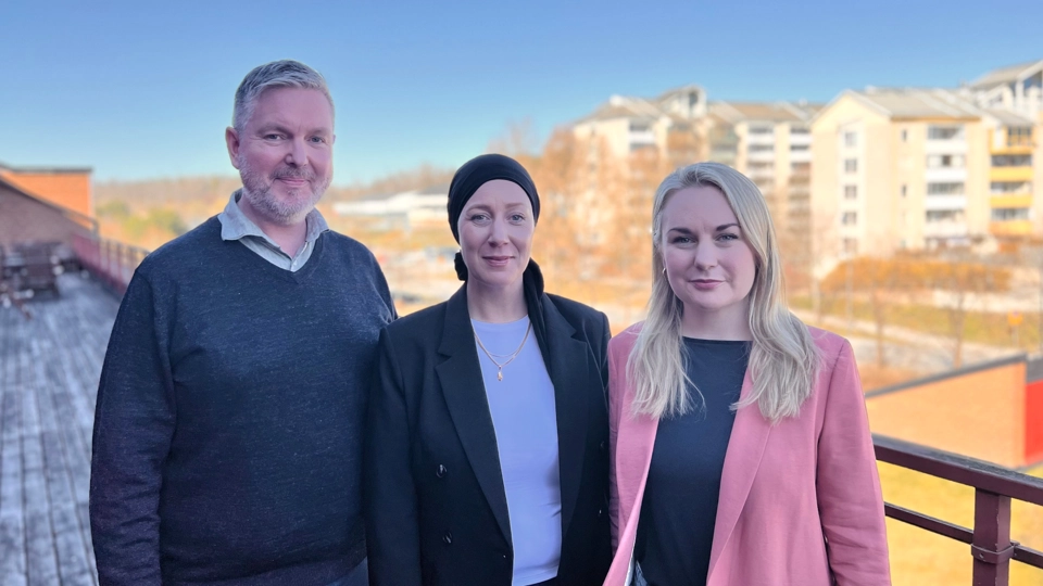 Johan står på en balkong på taket av Alceahuset och till höger om honom står Johanna och Linn från SOS barnbyar. Bakom dem syns höghus.