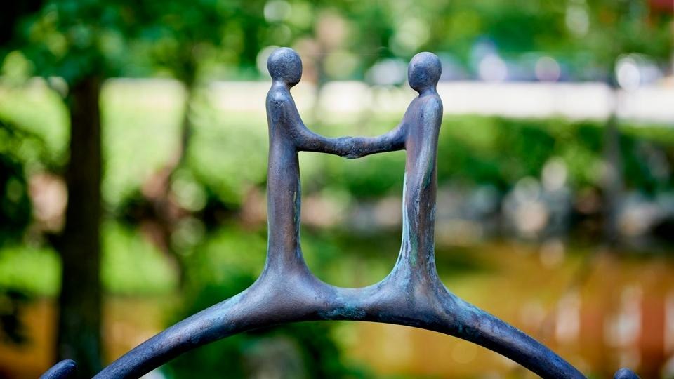 Konstverk som visar två figurer som sträcker armarna mot varandra formade som en bro.