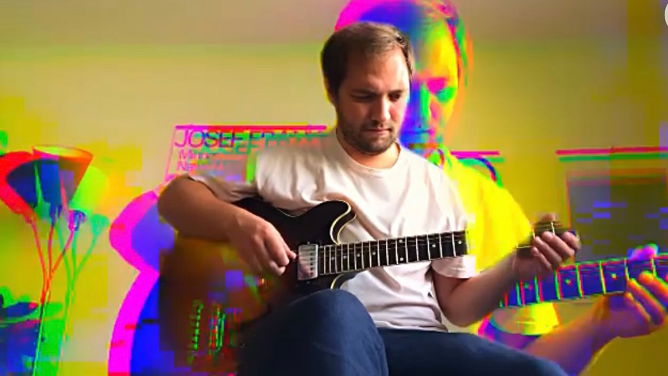 En man i t-shirt spelar gitarr.