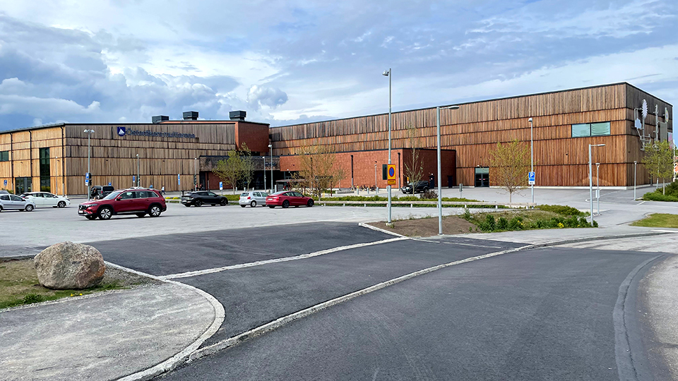 Nyasfalterat infart till parkering framför en idrottshall i trä